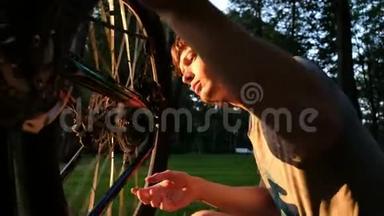 一个人骑着一辆上翻的自行车转动轮子，那个人在公园里的日落时修理辐条